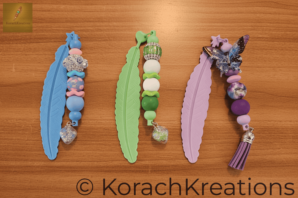 Overhead flat lay of 3 beaded bookmarks arranged side by side on a warm wooden library counter, all beads and tassel designs clearly visible